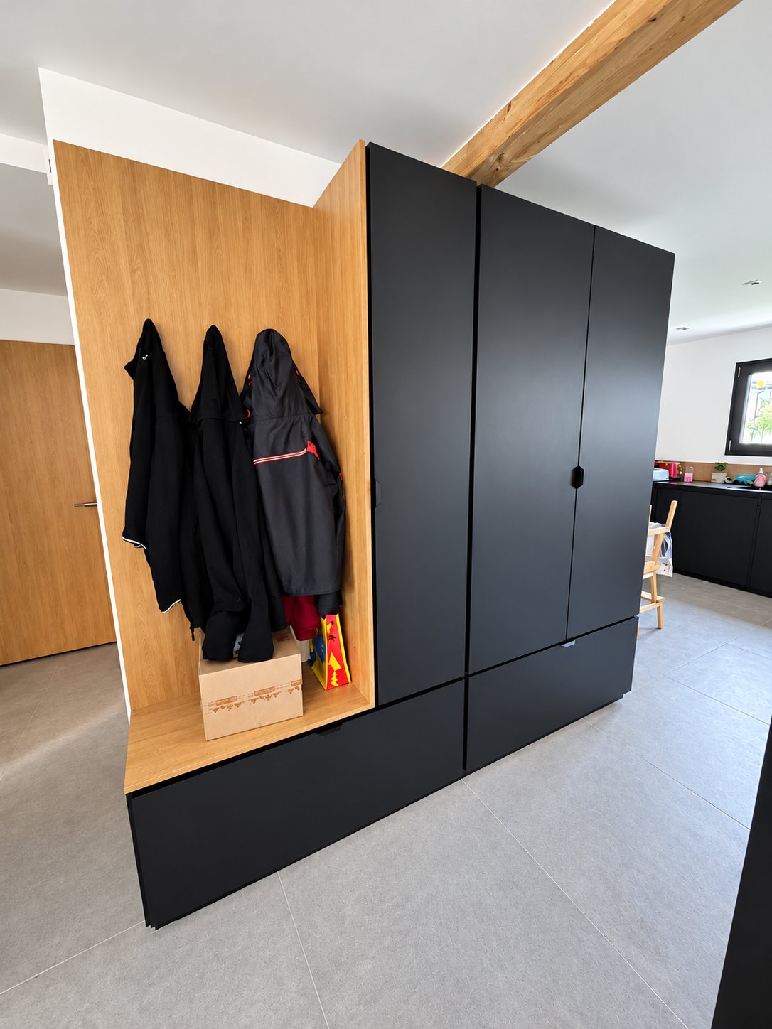 Placard d'entrée sur mesure aux façades noires mates et à l'intérieur en bois clair, avec des manteaux suspendus.